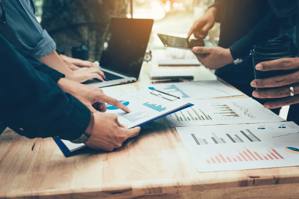 Réunion de travail en intérieur, deux personnes analysent des données financières sur une table en bois