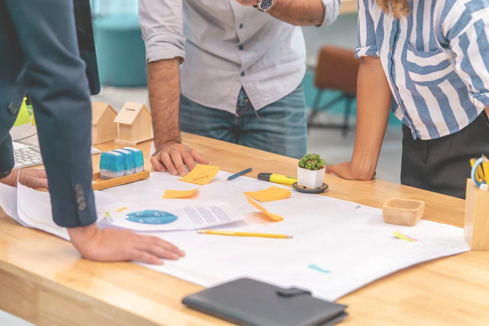 Réunion de travail collaborative dans un bureau moderne avec trois personnes debout autour d'une table en bois