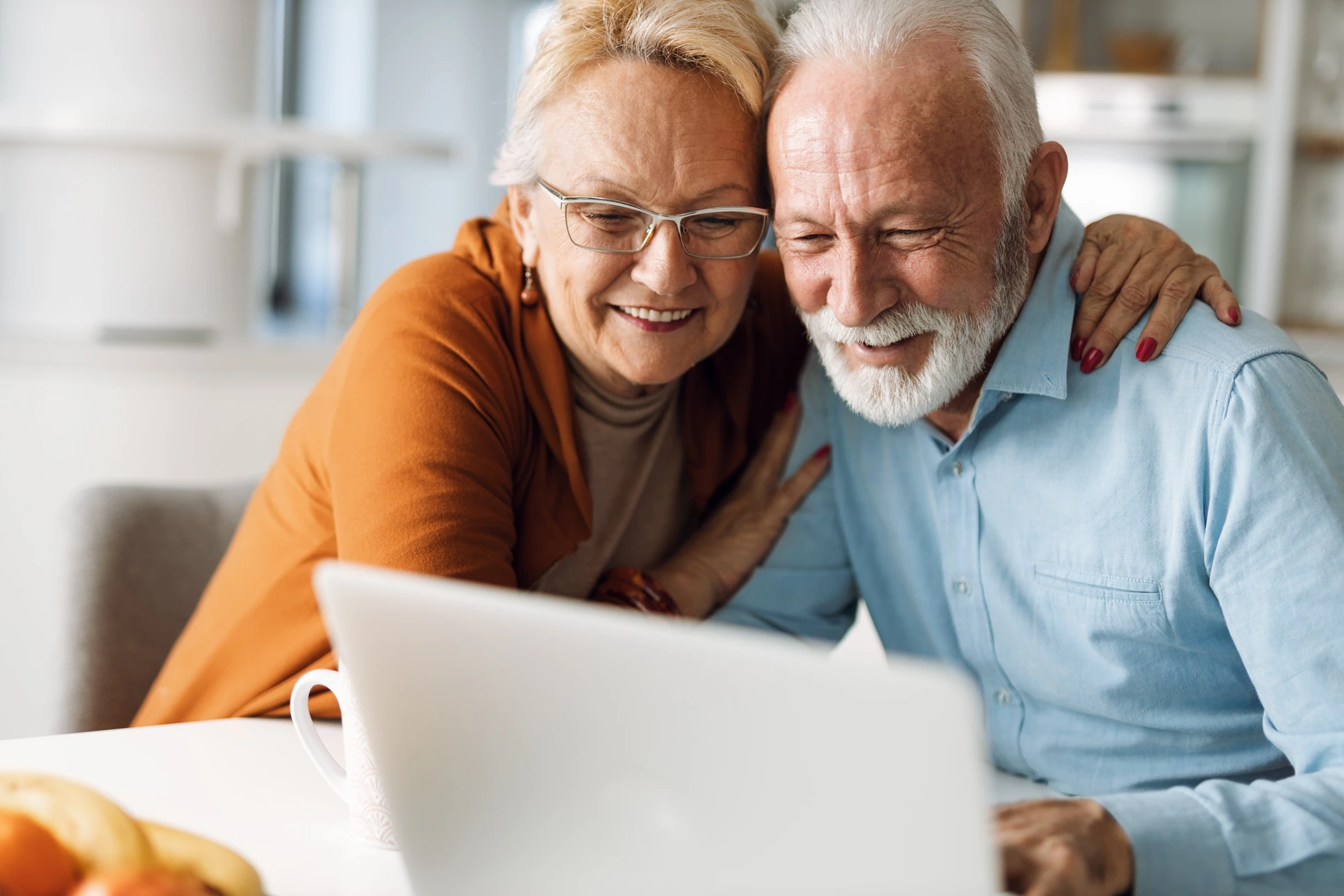 Couple de seniors souriants regardant ensemble un ordinateur portable dans un intérieur moderne