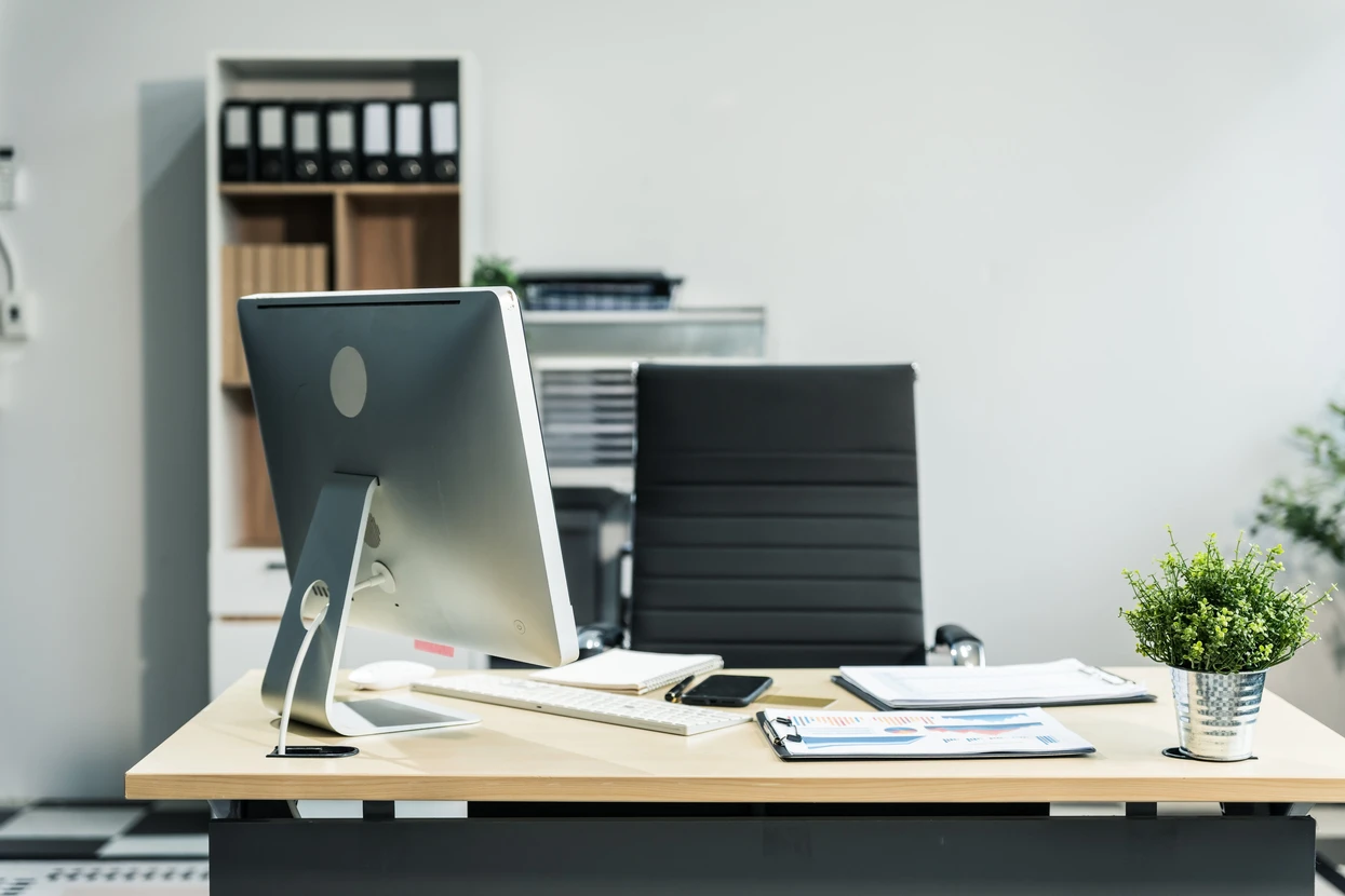 Un bureau moderne de couleur blanche avec un bureau en bois, une calculatrice, un ordinateur de bureau et une chaise en cuir noir