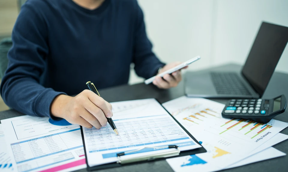 Femme professionnelle travaillant à domicile, consultant des documents financiers sur ordinateur portable tout en utilisant une calculatrice